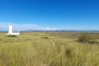 A lighthouse with grass in the foreground and a bright blue sky