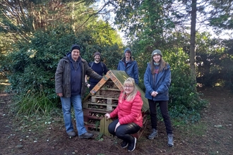 5 people standing around a bug hotel in a woodland