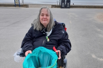 Woman sits in mobility scooter on Fleetwood promenade with bag of litter