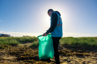 Man picking litter on beach with sun behind him