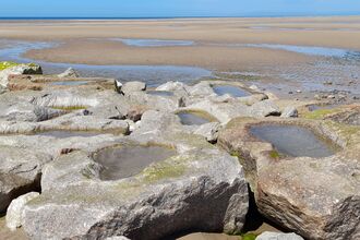Small pools of water in large rocks at the end of a rocky groyne. The sea is out and sand can be seen behind these artificial rock pools
