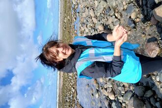 A lady holding a worm on a beach.