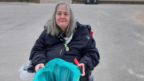 Woman sits in mobility scooter on Fleetwood promenade with bag of litter