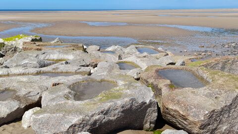 Small pools of water in large rocks at the end of a rocky groyne. The sea is out and sand can be seen behind these artificial rock pools