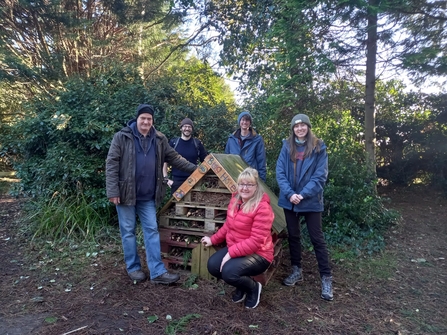 5 people standing around a bug hotel in a woodland