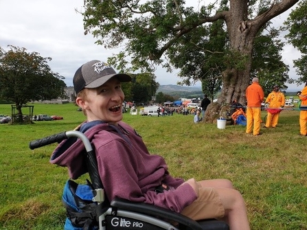 A young man in a wheelchair wearing a baseball cap and smiling