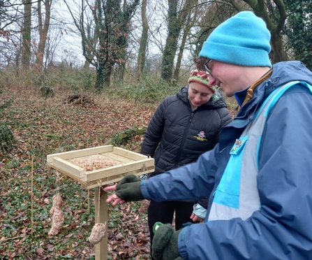 Two people hanging bird feeders from a bird table