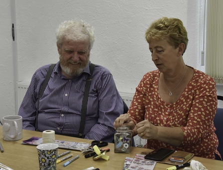 Two people decorate a jar with flowers