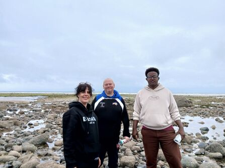 Three people on a stony beach.