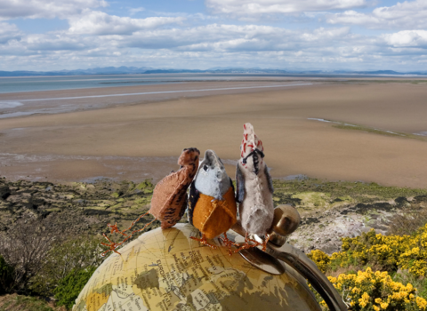 3 felt birds on a globe with a beach background